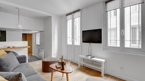 A modern living room with a grey sofa, a wooden coffee table with a bottle and glass, a white TV stand, and large windows. - TBS 342 - Superb apartment in the heart of Paris 2 (Paris)
