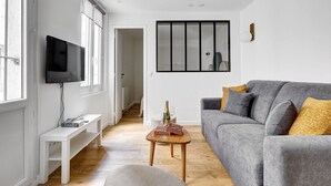 A modern living room with a grey sofa, wooden flooring, a TV on the wall, and a small table with a bottle and glasses. - TBS 342 - Superb apartment in the heart of Paris 2 (Paris)