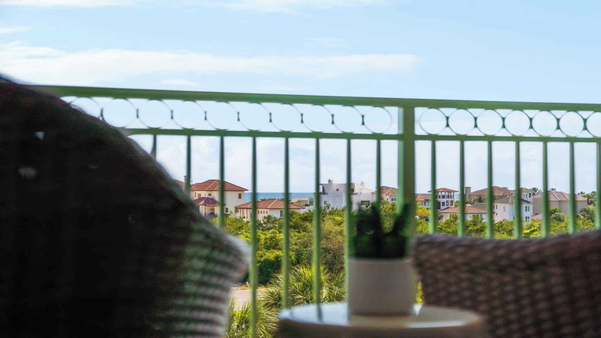 A balcony with a green metal railing, a potted plant, and a view of residential buildings.