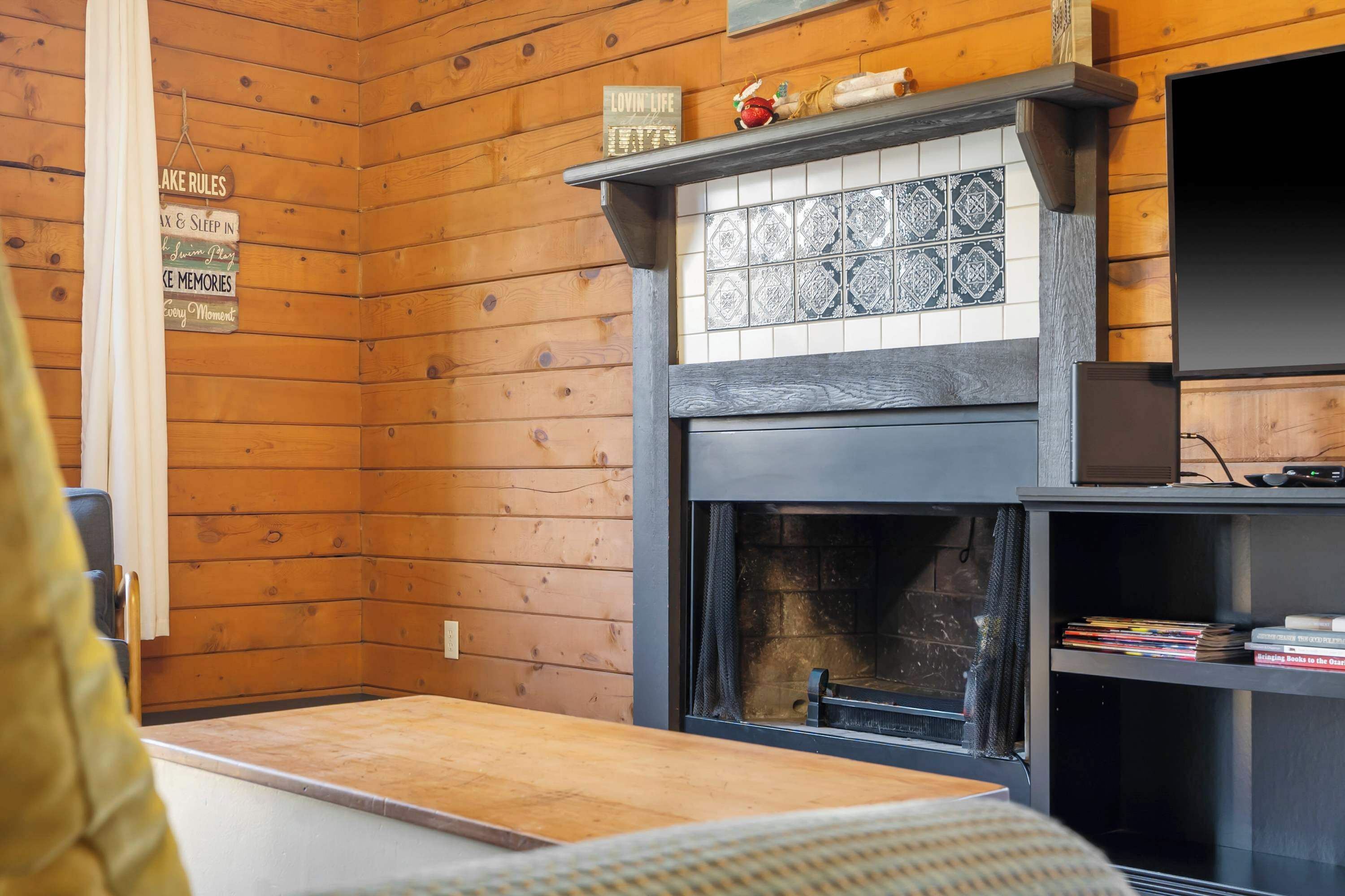 A cozy cabin interior with a fireplace, wooden walls, and a shelf with books.