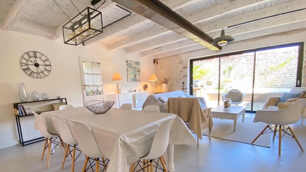 Un ampio soggiorno con soffitto alto, un'area pranzo con tavolo e sedie bianche e una grande finestra che offre luce naturale.