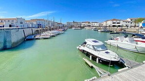 Una marina con imbarcazioni ormeggiate lungo una banchina, circondata da edifici con balconi e un cielo azzurro intenso.