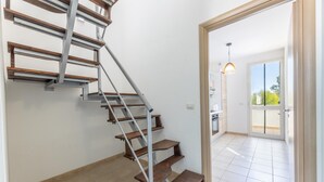 Eine moderne Treppe mit Holzdielen und Metallgeländern, die zu einem Raum mit einem großen Fenster und einer Tür in einen Außenbereich führt.