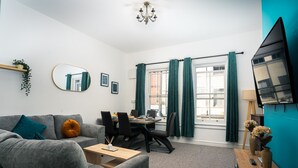 A modern living room with a grey sofa, a wooden coffee table, and a dining area with a table and chairs. - Central YeovilStay|Contractors|Free Wi-Fi|Sleeps 8 (Yeovil)