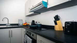 A modern kitchen with white cabinets, a black countertop, a stainless steel range hood, a kettle, a toaster, and a knife block. - Central YeovilStay|Contractors|Free Wi-Fi|Sleeps 8 (Yeovil)