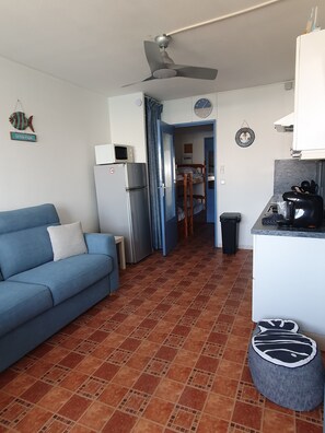A compact living space with a kitchenette, a blue sofa, a tiled floor, and a ceiling fan. - Studio sea view Ile des Pêcheurs (Agde)