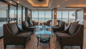 A spacious indoor area with large windows offering a view of the ocean, furnished with comfortable seating and a central glass table. - Cozy studio in charming Myrtle Beach with refreshing oceans view (Myrtle Beach)