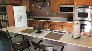 Una cocina con armarios de madera, un refrigerador, un microondas, un horno y un comedor con sillas y una isla central.