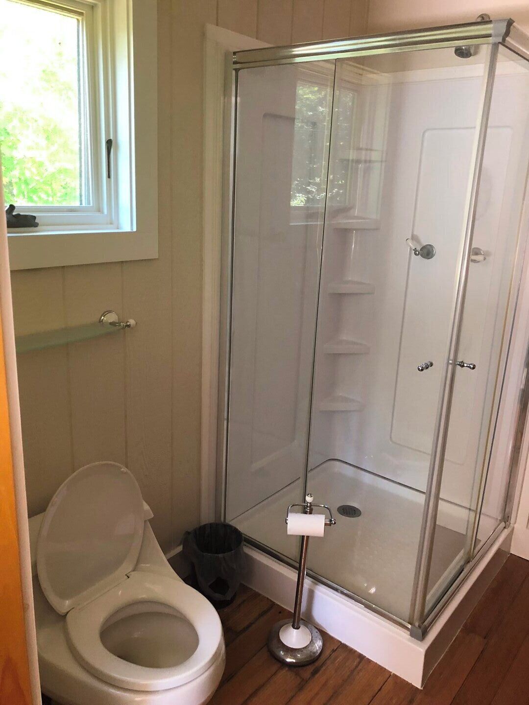 Une salle de bain avec des toilettes, une douche à parois de verre et une fenêtre.