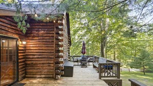 Una cabaña de madera con terraza, mobiliario exterior y vistas al bosque circundante.