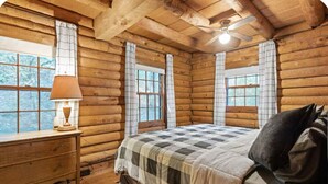 Un dormitorio tipo cabaña de madera con una cama, una mesita de noche, una lámpara y un ventilador de techo.