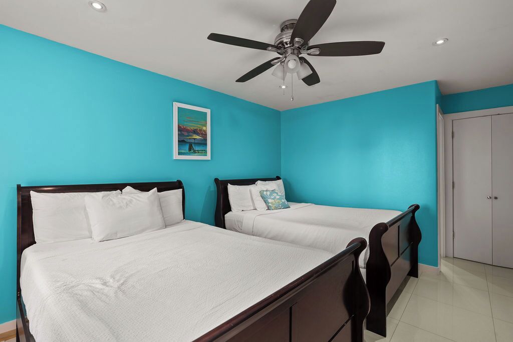 Una habitación con dos camas, un ventilador de techo y una puerta.