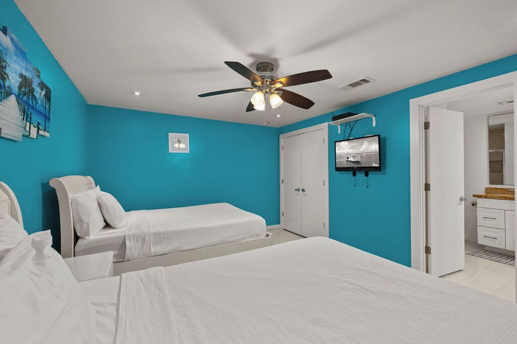 A bedroom with two beds, a ceiling fan, a TV, and a bathroom visible through an open door.