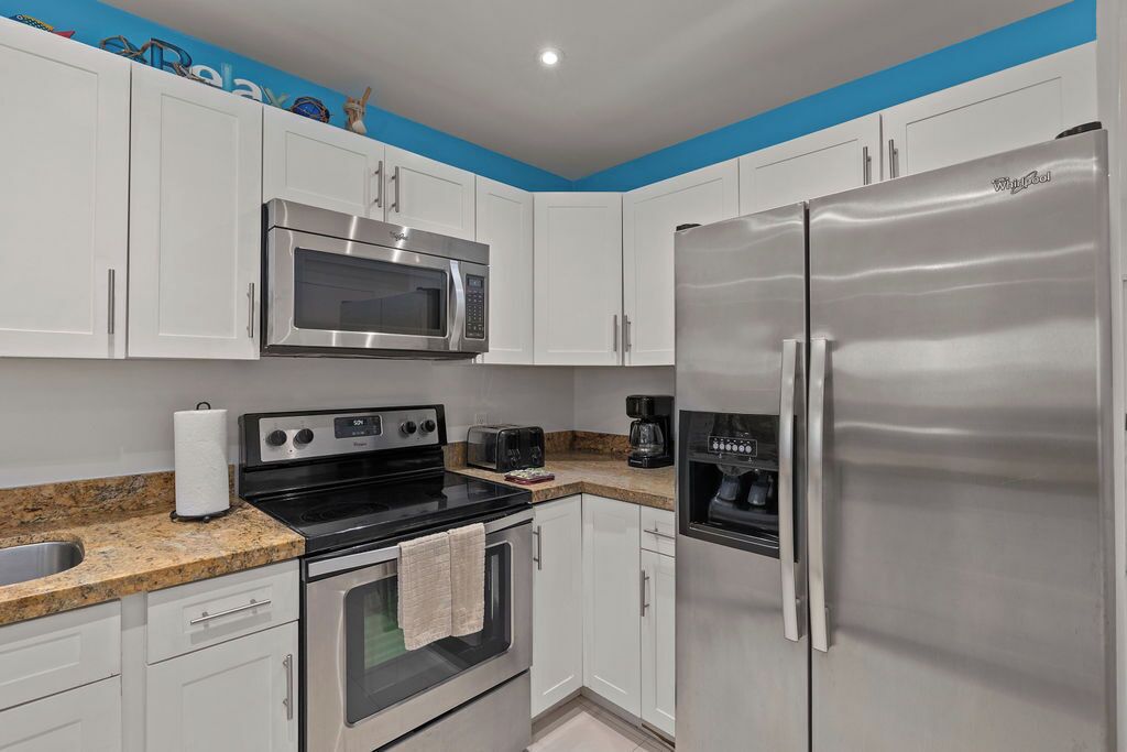 A modern kitchen with white cabinets, a stainless steel refrigerator, a microwave, a stove, and a coffee maker.