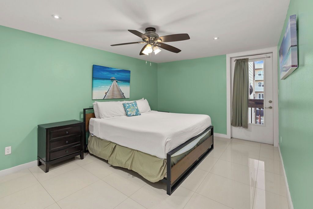 A bedroom with a bed, a nightstand, a ceiling fan, and a painting of a pier.