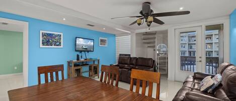 Un coin repas avec une table et des chaises en bois, un ventilateur de plafond et un téléviseur fixé au mur.