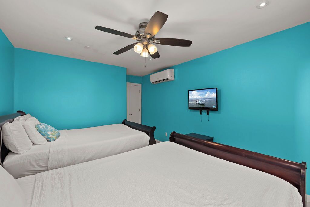 Ein Zimmer mit zwei Betten, einem Deckenventilator, einer Klimaanlage und einem Wand-Fernseher.