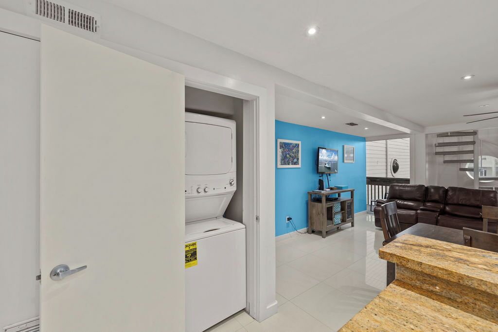 A modern living room with a white washing machine, a blue accent wall, a TV, and a leather couch.