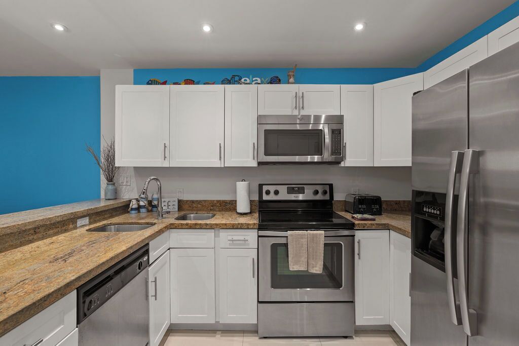 A modern kitchen with white cabinets, a stainless steel refrigerator, a microwave, an oven, and a sink.