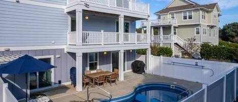 A two-story house with a backyard swimming pool, a covered patio with a table and chairs, and a covered grill area.