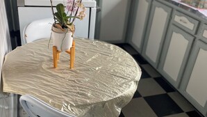 Una cocina con una mesa redonda cubierta con plástico, un microondas, un hervidor y una planta en maceta.