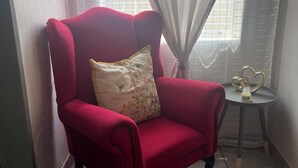 Un sillón rojo con un cojín floral en un rincón con una mesita y un objeto decorativo.