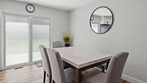 A dining area with a marble table, four grey chairs, a round mirror, and a clock on the wall.