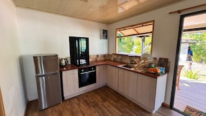 Une cuisine de taille réduite, dotée de meubles en bois, d’un réfrigérateur en acier inoxydable, d’une cuisinière noire et d’une fenêtre donnant sur un paysage verdoyant.