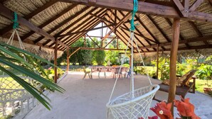 Un espace extérieur abrité comprenant une balançoire, une table avec des chaises et une vue sur le jardin.