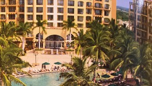Ein Poolbereich eines Resorts mit mehreren Schwimmbecken, Palmen und einem großen Hotel im Hintergrund.