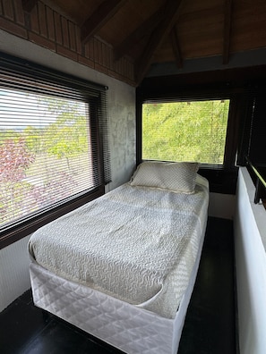 A single bed with a quilted mattress in a room with wooden beams on the ceiling.