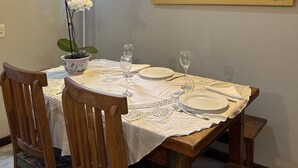 Ένας χώρος τραπεζαρίας με ένα τραπέζι στρωμένο για τέσσερα άτομα, ξύλινες καρέκλες, μια ορχιδέα σε γλάστρα και έναν πίνακα στον τοίχο.