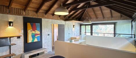 A spacious room with a high ceiling, a large bed, a desk, and a window providing a view of the outdoors.