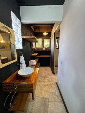 A narrow bathroom with a wooden vanity, a large mirror, and a window with a view of greenery.