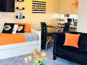 Un salon moderne avec un canapé blanc, des coussins orange, un fauteuil noir et un coin repas doté d’une table en verre.