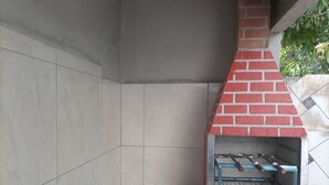 A brick-built outdoor grill with a tiled floor and a metal rack for grilling. - House in Guriri for rent (SAO MATEUS)