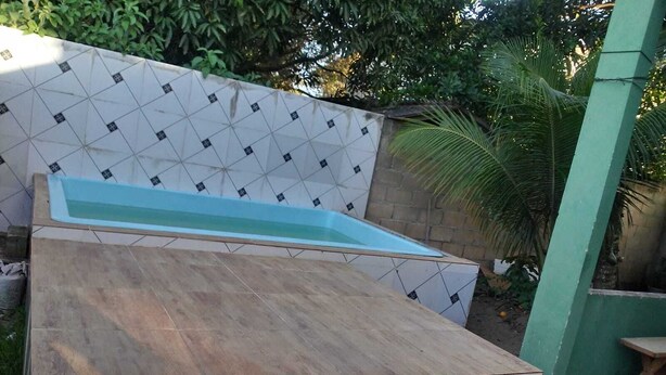 A swimming pool with a geometric tile pattern on the walls, surrounded by greenery and a stone wall. - House in Guriri for rent (SAO MATEUS)