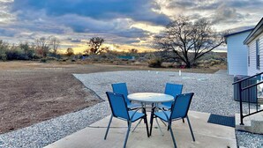 An outdoor patio with a round table and four blue chairs, surrounded by gravel and a concrete border. - Four Corners Retreat! Spacious 4-bedroom house in Aztec, NM. (Aztec)