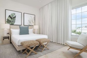 A modern bedroom with a bed, two bedside tables, a chair, and a large window. - 2-Min Walk to Grace Bay Beach Condo (Grace Bay)