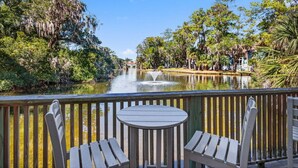A wooden deck with a table and chairs overlooking a calm river, surrounded by lush greenery and trees. - Pet Friendly, Tiki Bar, 3 pools, pickleball! (Edisto Island)