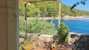 A wooden table with a vase of flowers, a stone wall, and a view of a lake with boats. - Apartments Stiniva Hvar (Hvar)
