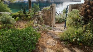 A stone pathway leading to a rustic stone structure with a view of a calm lake and boats. - Apartments Stiniva Hvar (Hvar)