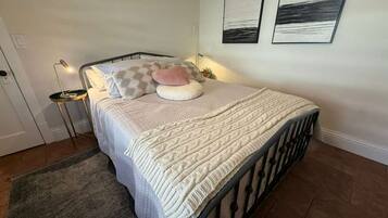 Een net opgemaakt bed met een bedsprei en kussens, een bedlampje en twee ingelijste kunstwerken aan de muur.