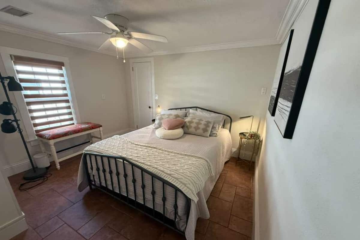 A bedroom with a bed, a bench, a ceiling fan, and a window with blinds.