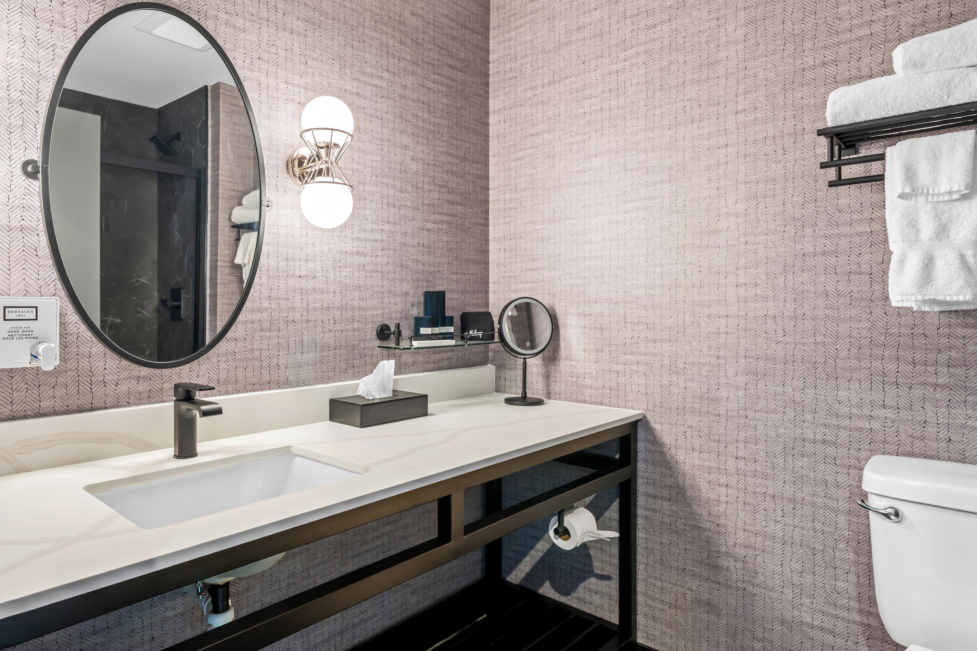 A bathroom with a large mirror, a sink, a towel rack, and a toilet.