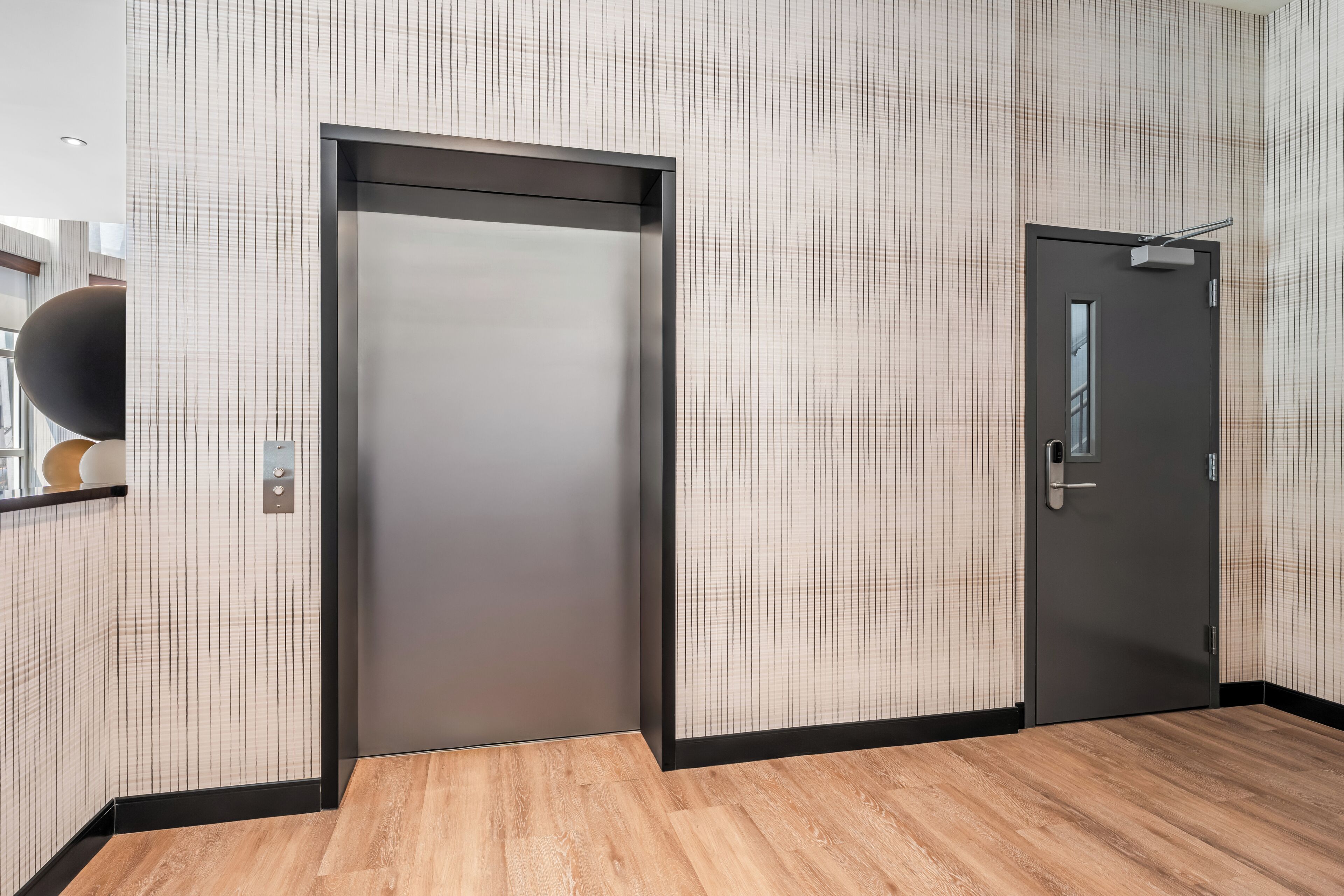 Un ascenseur moderne aux finitions métalliques, situé à côté d’une porte dotée d’une poignée et d’une petite fenêtre.