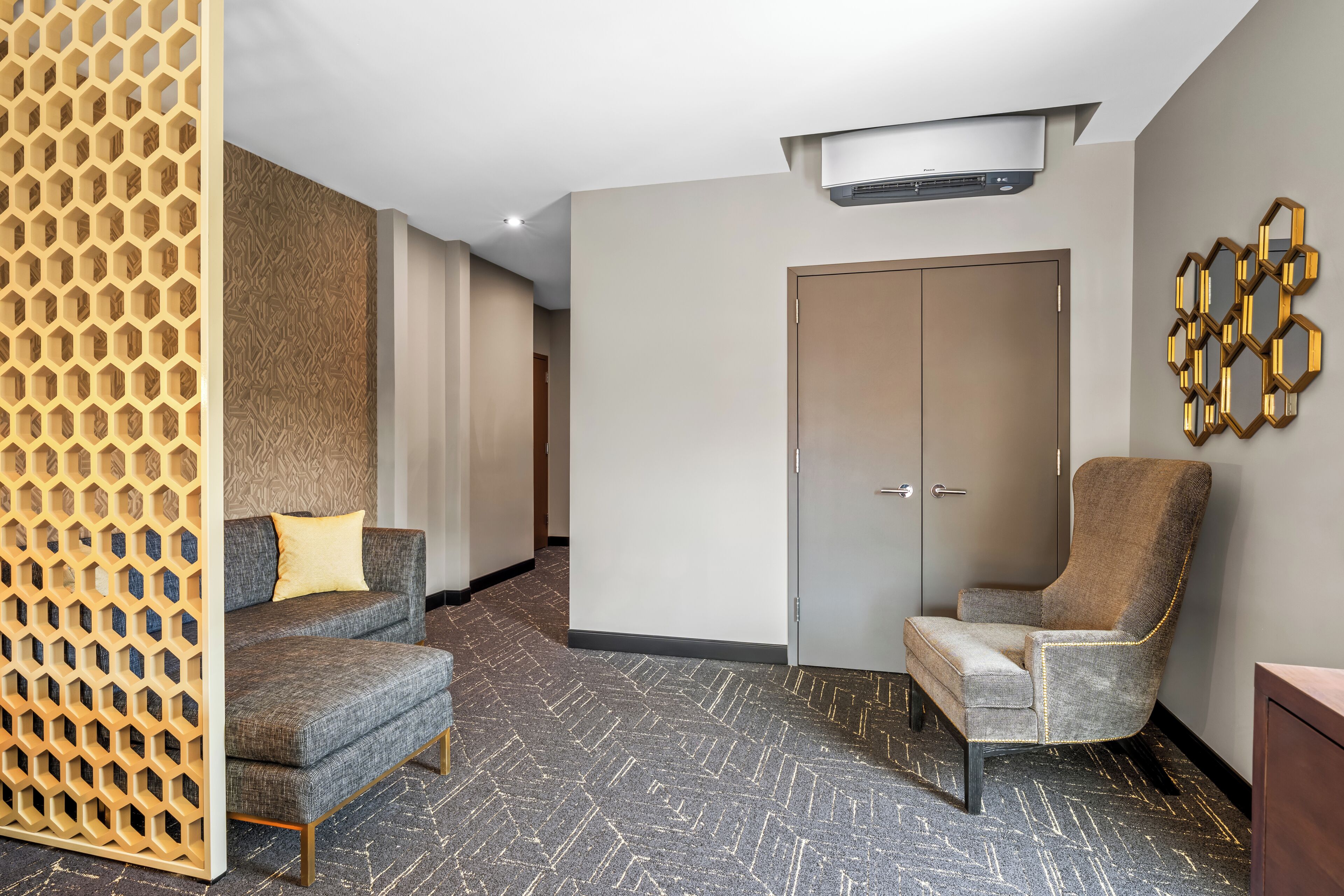 Habitación de hotel con alfombra estampada, un sofá, una silla, un armario y un adorno de pared.