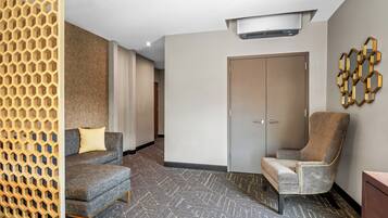 Habitación de hotel con alfombra estampada, un sofá, una silla, un armario y un adorno de pared.