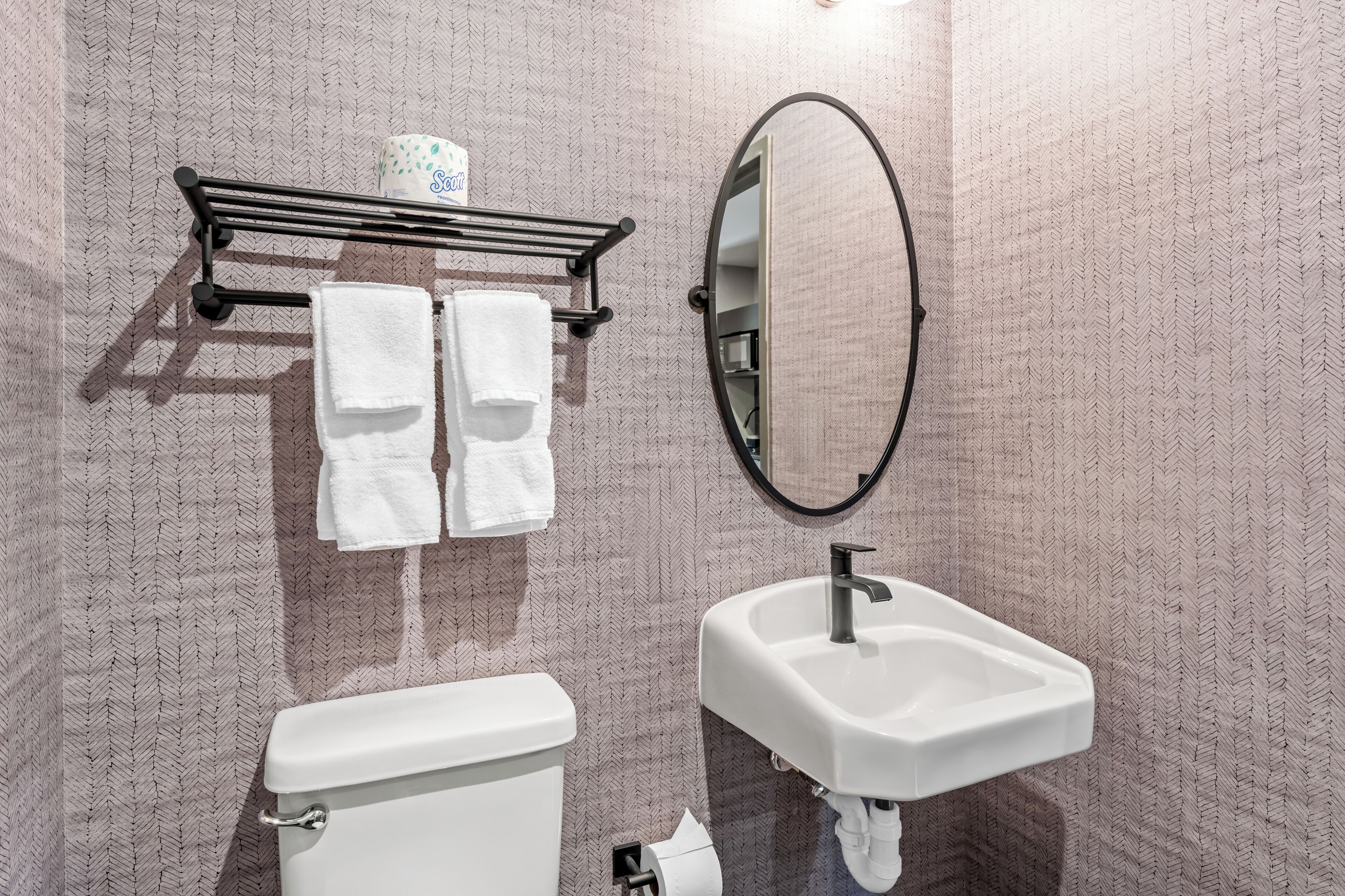 A bathroom with a toilet, sink, towel rack, and a mirror.