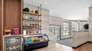Un hall d’hôtel moderne doté d’une vitrine réfrigérée, d’un comptoir d’accueil en bois et d’une étagère murale où sont exposés divers objets.